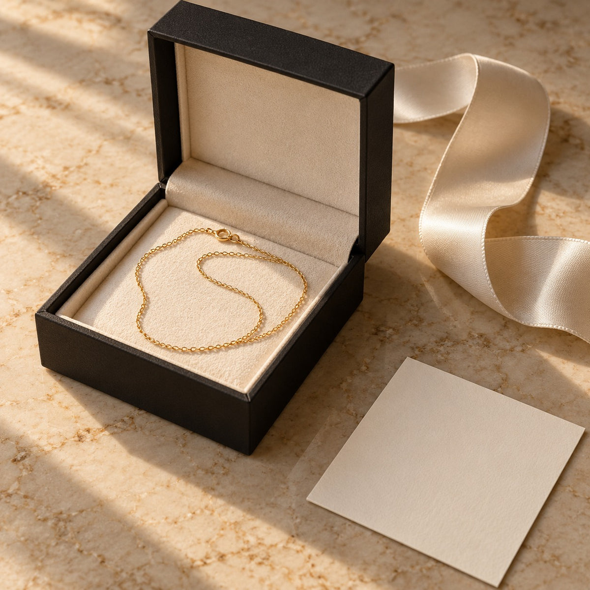 Écrin ouvert, ruban de satin et carte, sur marbre beige